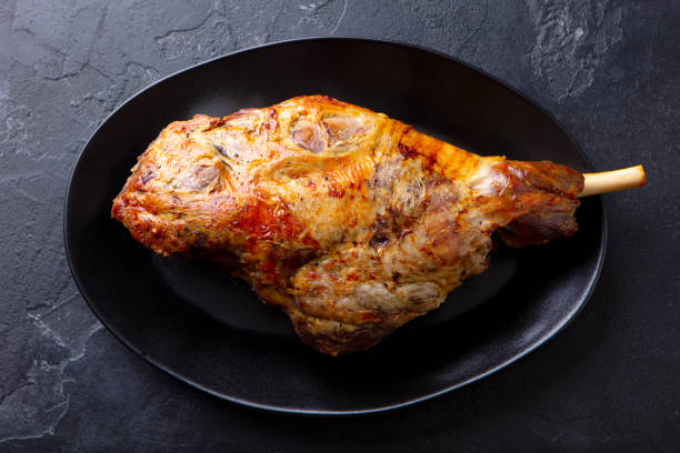 istock Roasted lamb leg on a plate. Black background. Close up. Top view. 1264801138