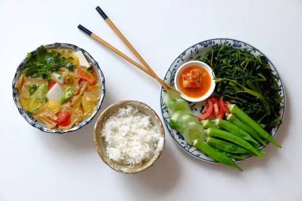 Top view vegan daily meal for lunch time, boiled okra, water spinach, cucumber with tofu cheese, rice bowl, vegetables soup with tofu skin, simple vegetarian Vietnamese food for healthy diet