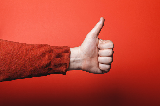Man hand shows thumb up on red background.