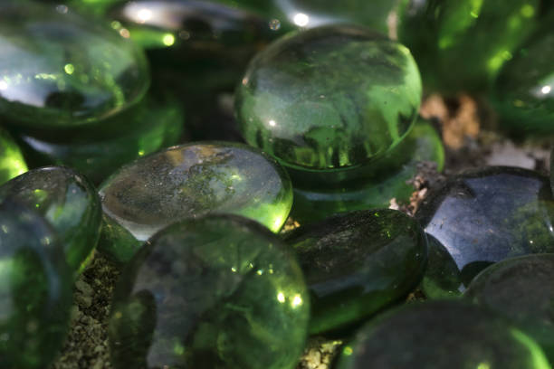 These are dark, round glass pebbles laid on bare earth in order to discourage the growth of weeds and other plants. Photographed here in close up, outdoors, and glistening in sunlight.