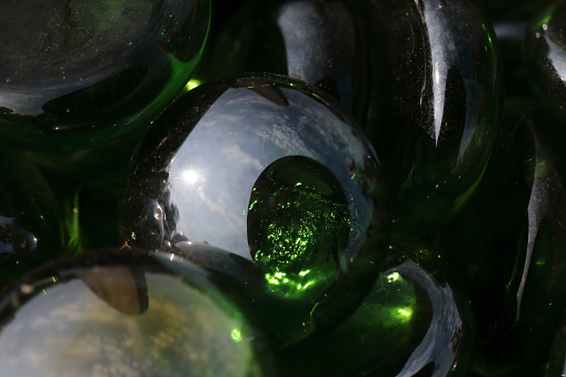 These are dark, round glass pebbles laid on bare earth in order to discourage the growth of weeds and other plants. Photographed here in close up, outdoors, and glistening in sunlight.