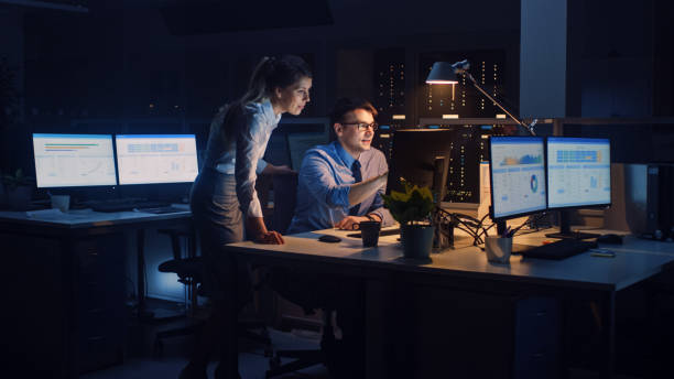 istock Ambitious and Confident Businessman Uses Desktop Computer, His Female Project Manager Explains Specific Tasks, Account Handling and Strategic Moves. Professional People Late in Big Corporate Office 1264819584