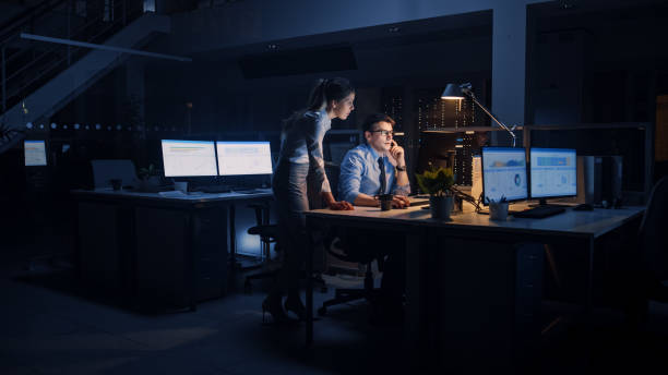 istock Ambitious and Confident Businessman Uses Desktop Computer, His Female Project Manager Explains Specific Tasks, Account Handling and Strategic Moves. People Late at Night in Big Corporate Office 1264819609
