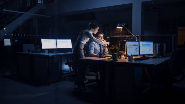 istock Ambitious, Confident Businessman Uses Desktop Computer, His Female Project Manager Explains Specific Tasks, Account Handling and Strategic Moves. Professional People Late at Night in Corporate Office 1264819641