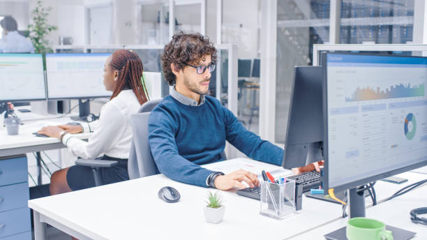 istock In the Big Busy Corporate Office Professional Worker Using Desktop Computer, Around Him Businesspeople and Experts Working with Clients, Having Discussions and Analysing Statistics 1264819664