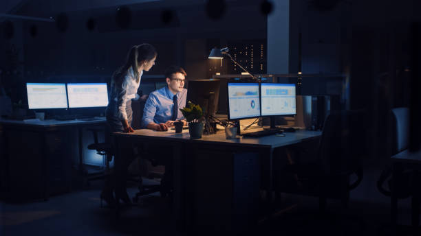 istock Ambitious, Confident Businessman Uses Desktop Computer, His Female Project Manager Explains Specific Tasks, Account Handling and Strategic Moves. Professional People Late at Night in Corporate Office 1264819690
