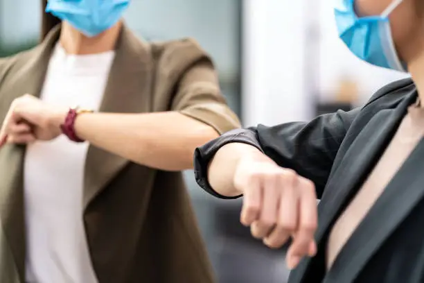 Close up two businesswomen do alternative greeting in new normal office lifestyle. They wear protective face mask and use elbow bump instead of handshake to reduce infection of coronavirus COVID-19.