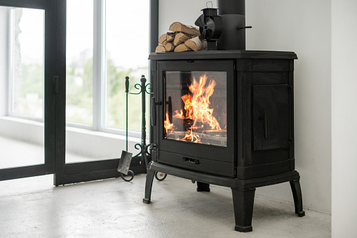 Fireplace at lounge room standing on concrete floor with copy space. Home with modern interior, wooden log on top of fireside and equipment against white wall