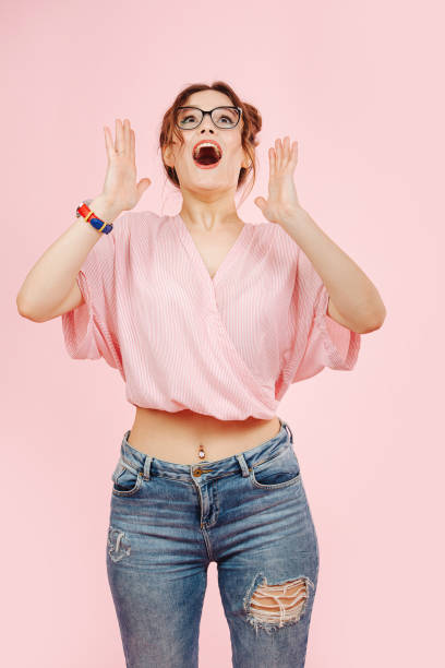 удивленный чрезмерно эмоциональный девушка в свободном розовом топе и джинсах смотрит вверх - overemotional стоковые фото и изображения