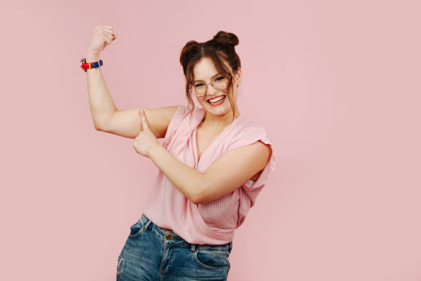 overemotional young woman in glasses pointing on her strong biceps and smiling - overemotional imagens e fotografias de stock