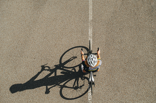 Top view of a young ginger woman riding on a professional bike. She's geared up, wearing helmet and cycling jersey. On a blazing hot sunny day.