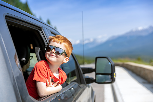 Young cute redhead child leaning on the car window and Contemplating the views while on road trip