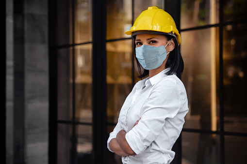 Portrait of a Confident Construction Engineer Woman. Wearing Surgical Protection Mask and Looking at Camera. Standing in front of the Modern Office Building