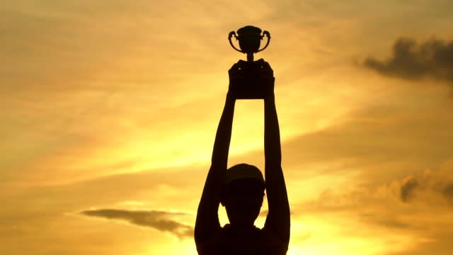 The winner holding a trophy at sunset silhouette