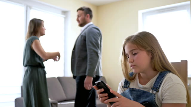 Family scandal. Parents quarrel ignoring their daughter. A teenage girl tries to distract herself using a mobile phone