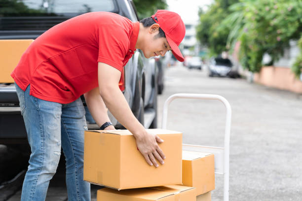 asian delivery man wearing red uniform and red hat moving and transfer parcel boxes. concept of express delivery, transportation, online shopping - mail van imagens e fotografias de stock