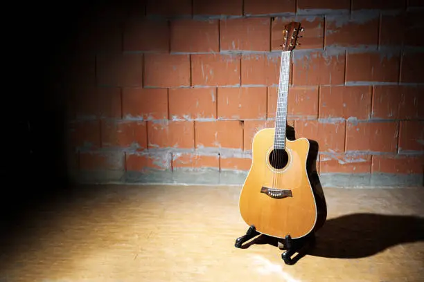 Photo of Acoustic guitar in front of a raw brick wall in the rehearsal studio of a garage band, copy space
