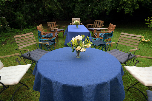 Set up for a family garden party with tables, blue tablecloths and different chairs on the lawn in a rural backyard, selected focus