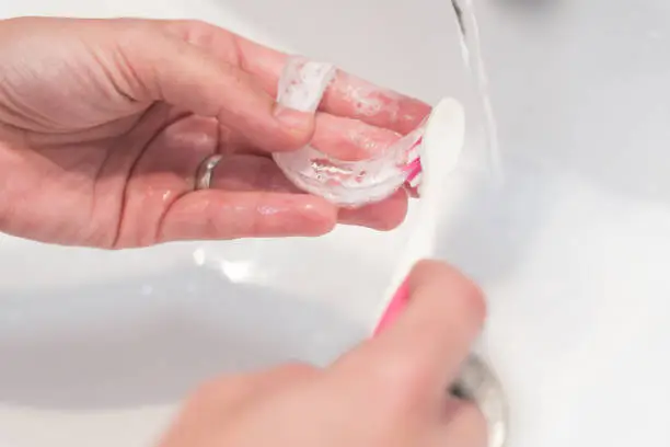 woman's hands washing her invisible aligners for dental correction with soap and water