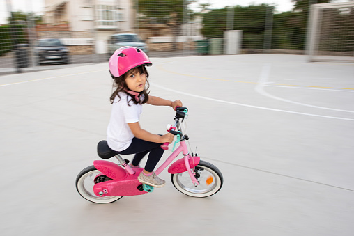 a little girl cycling on a pink bike in a park.