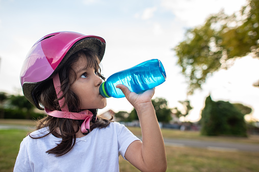 5 years old girl drinking water from a bottle after a bike ride.