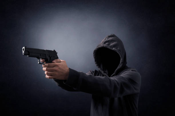 istock Hooded man with a gun in the dark 1264872092