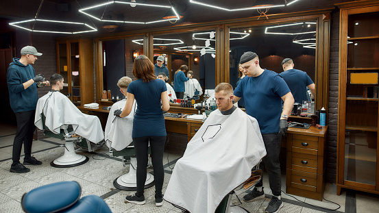 Working process. Three professional barbers serving clients in the modern loft style barbershop. Hairdresser services. People visiting hair salon. Barber Shop interior