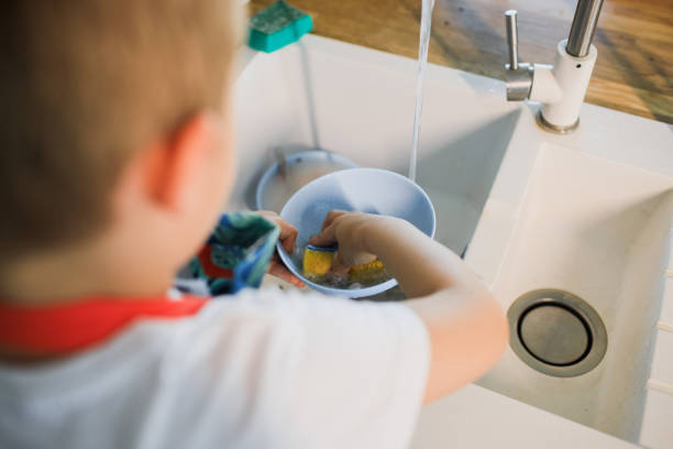 istock a little boy washes dishes in a modern kitchen 1264889382