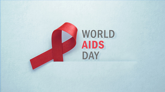 Red AIDS awareness ribbon sitting next to World AIDS Day message on gray background. Horizontal composition with copy space. World AIDS Day concept.