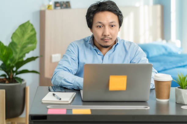 istock Asian business man using technology laptop and working from home with surprise action in bedroom of house by video conference call 1264927914