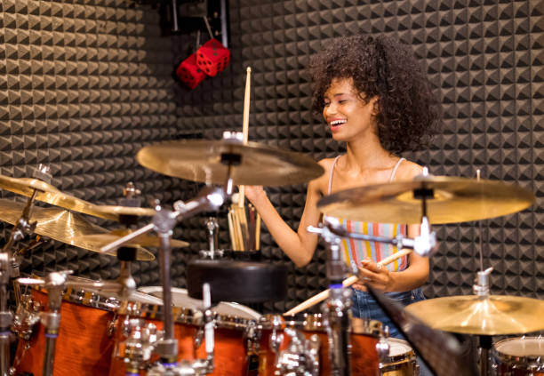 Laughing vivacious young woman playing drums Laughing happy vivacious young Afro American woman in her twenties seated playing drums and cymbals in a studio drummer stock pictures, royalty-free photos & images