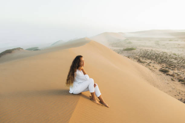 モロッコサハラ砂漠の砂丘の上でリラックス白い服を着た美しいブルネットの女性。日の出前の朝の霧。自然との調和 - desert landscape morocco sand dune ストックフォトと画像