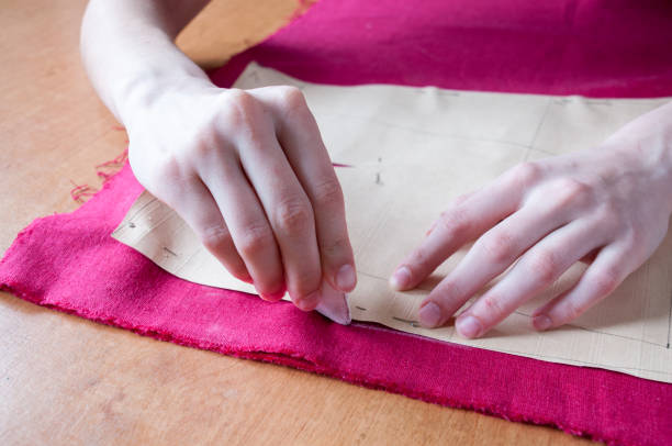 istock Women's hands trace a small paper pattern on a red cloth on the table 1264934326