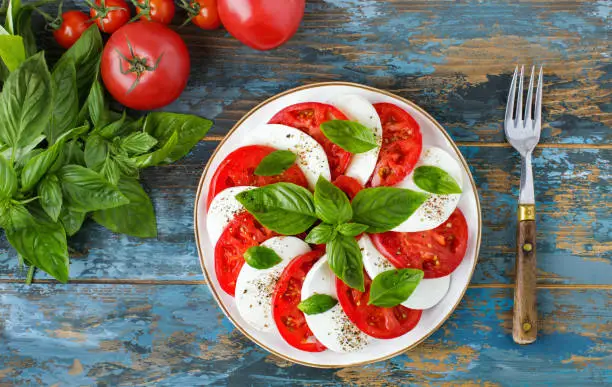 Caprese salad with mozzarella and Basil tomatoes on a wooden background, top view, diet