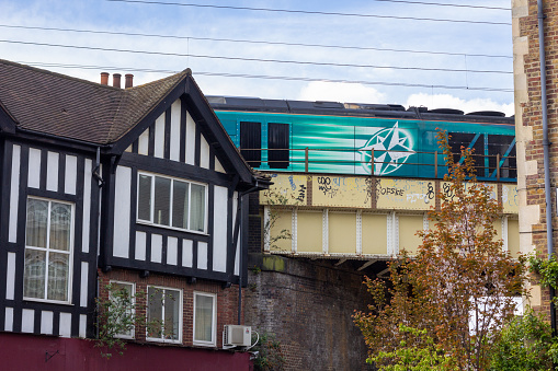 A train with a recognisable logo whizzes past Hartland Road in Camden, London. There is also graffiti in the background.