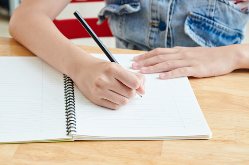 Close-up image of schoolgirl writing essay in copybook at her desk or drawing sketch for school project