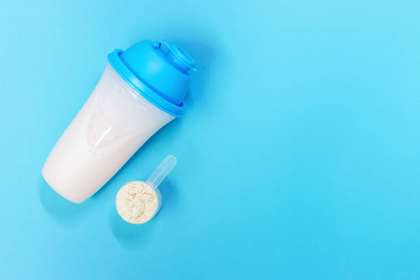protein shake and measuring spoon with powdered protein on blue background, a copy of the space - body building milk shake protein drink drink imagens e fotografias de stock