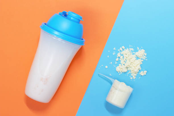 protein shake and measuring spoon with powdered protein on blue and orange background, a copy of the space - body building milk shake protein drink drink imagens e fotografias de stock