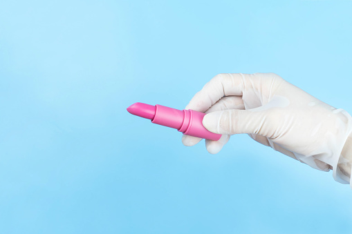Hand in white medical gloves holding punk lipstick on blue background