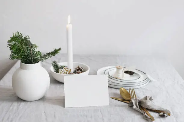 Traditional Christmas table place setting. Golden cutlery, fir tree branches in vase, plates and burning candle in ceramic candleholder on linen table cloth, holidays background. Place card mockup