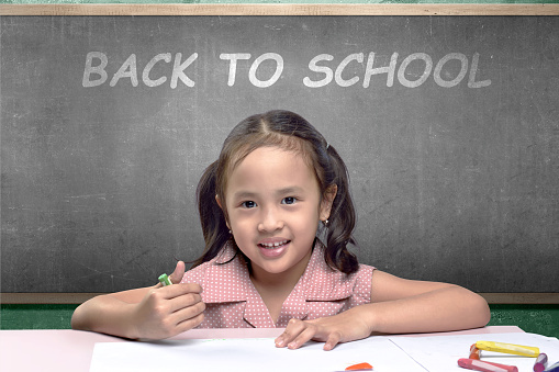 Asian little girl with a crayon drawing in the paper on the table. Back to School concept