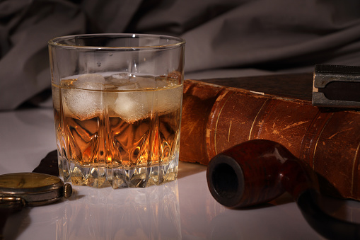 Close-up of a glass of whiskey on a rustic wooden table. A bottle of scotch whiskey can be seen in the background.