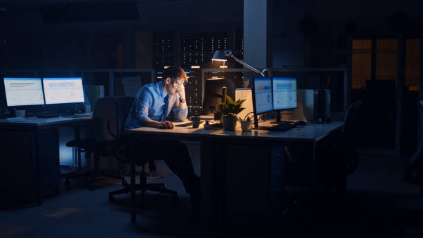 in ufficio di notte, l'impiegato stanco troppo stanco utilizza il computer desktop, strofina gli occhi stanchi. stanco frustrato uomo d'affari esausto addormentarsi al suo lavoro. - working late working computer busy foto e immagini stock