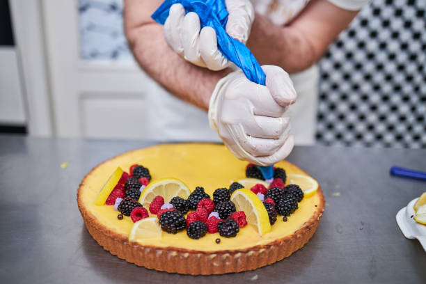 Professional confectioner decorating lemon custard cake with whipped cream