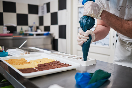 Professional confectioner squeezing chocolate mus from bag tube into a cake mold in his modern commercial kitchen