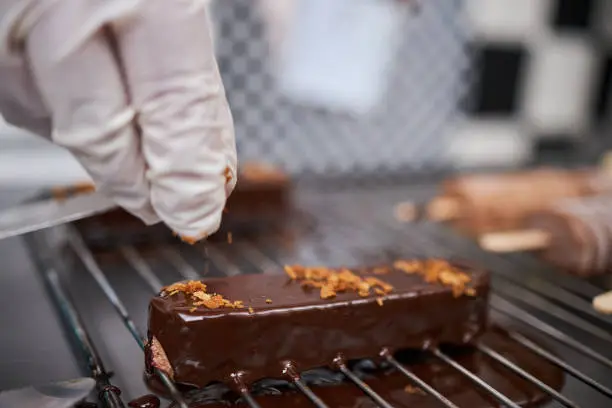 Professional confectioner sprinkle almond leaf on a chocolate cake biscuit on a metal net tray in cake factory