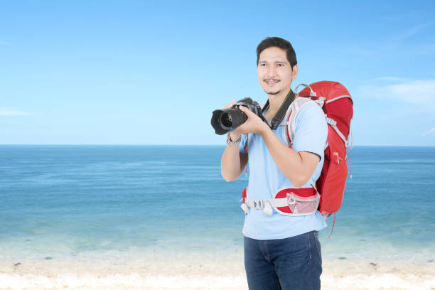 istock Asian man with a backpack holding the camera on the beach 1264974605