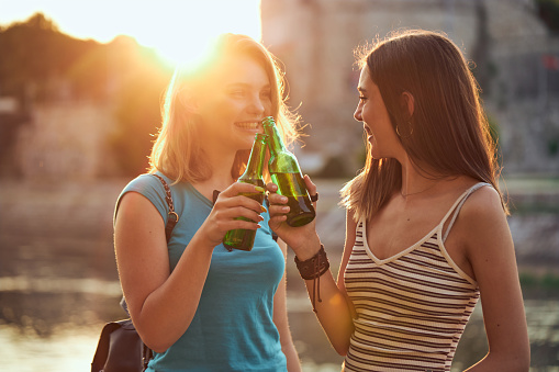 Carefree young women drinking cold beer while enjoying sunest on a qusyside on a hot summer day