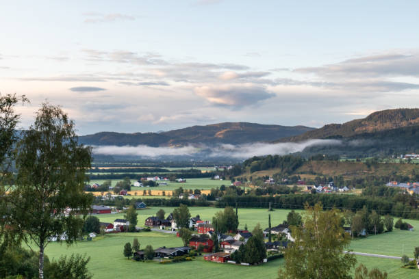 Rural Norway countryside morning sunrise view. Nice small nordic houses, green grass fields, beautiful purple clouds landscape