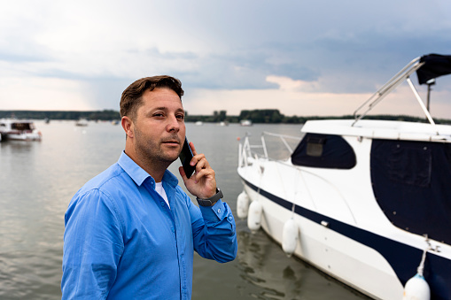 Man talking on the phone beside luxury yacht at port. Nautical and marine concept